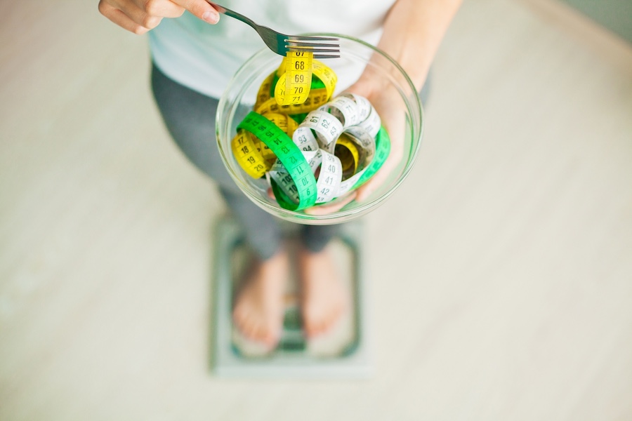 Jak schudnąć 20 kg w miesiąc? Zasady, dieta, przykładowy jadłospis Kobieta stojąca na wadze, miara w miseczce