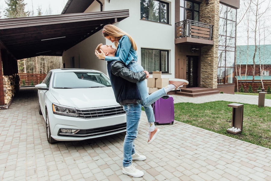 Kiedy wybrać carport zintegrowany z budynkiem? Mężczyzna unoszący kobietę, w tle samochód i dom z carportem