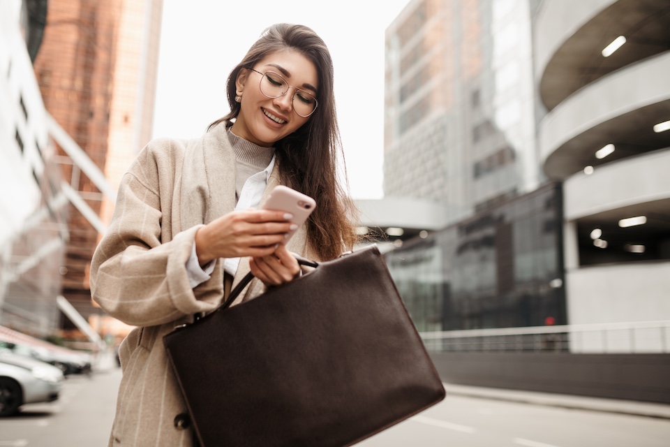 Rozbawiona kobieta z dużą torebką i smartfonem